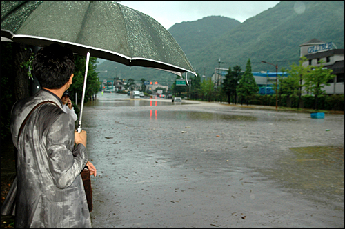 마산 봉암교 입구 3거리 도로가 16일 집중호우로 침수되어 트럭이 물 속에 잠긴 가운데, 시민들이 지켜보고 있다.