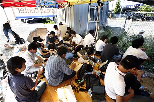 쌍용차 공장 정문 주변 주차장에 천막으로 만들어진 기자실에서 수십명의 기자들이 생수통박스 위에 노트북을 놓고 기사를 작성하고 있다. 