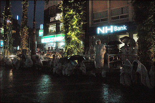 강정마을 주민 등 제주도민 200여 명이 폭우가 쏟아지고 있음에도 불구하고 얇은 비옷과 우산 아래 몸을 맡긴 채 서귀포시 1호광장에서 집회를 갖고 있다.