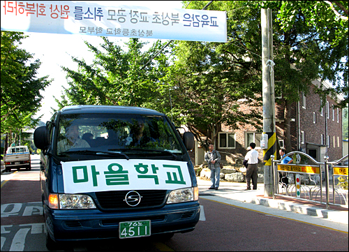  거창북상초교 학부모들은 교장공모 지정 취소 철회를 요구하며 1일부터 학생들을 등교시키지 않고 마을학교를 운영하고 있다. 사진은 마을학교 학생들을 통학시키는 승합차가 펼침막이 내걸린 도로를 달리는 모습.