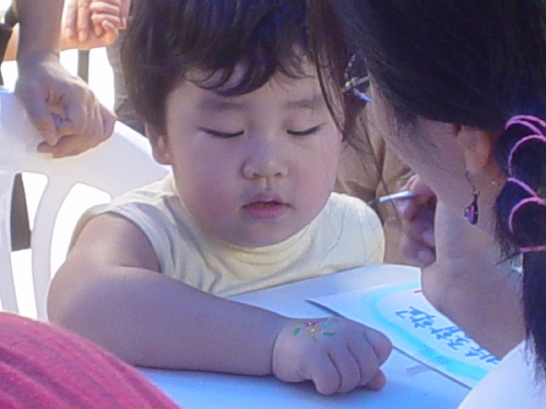 언론악법 원천무효를 위한 바자회장. 한 아이가 손에 그려진 꽃에서 눈을 뗄 줄 모르고 있다.