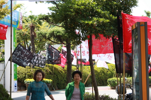 여수1청사 앞 천막농성장에 깃발이 펄럭이고 있는 가운데 시민들이 걸어가고 있다.