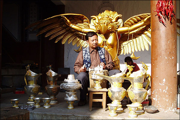 자신이 만든 작품을 배경으로 포즈를 취한 춘 장인. 리장 위쉐이자이(玉水寨)에 있는 동파신조는 춘 장인의 대표작 중 하나다.