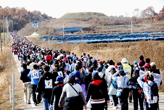 오른쪽위의 언덕에서 한국군 초병이 지켜보는 가운데 민통선을 걷고 있는 트레킹 참가자들


