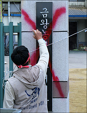  음성군쌀대책위 관계자가 금왕농협미곡처리장 이름 위에 붉은 색 페인트로 X표시를 하고있다. 