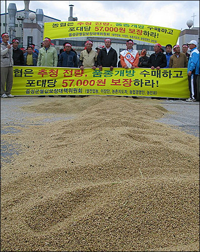  아스팔트 위에 뿌려진 벼를 바라보며 농민들이 기자회견을 준비하고 있다.