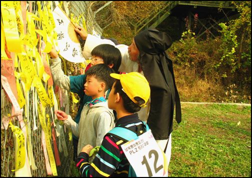 DMZ 걷기 대회에 참가하여 자신의 소원을 노랑 리본에 담아 손자 아이와 친구들이 서예가 김 일명 선생님과 함께 철책에 다는 모습
