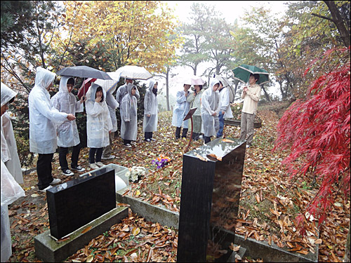 비가 내리는 가운데, 대학생들이 열사의 묘역을 둘러보며 설명을 듣고 있다.
