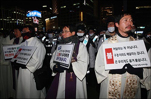 천주교정의구현전국사제단 신부들이 2일 밤 서울광장에서 열린 '죽은 자들과 죽어가는 뭇 생명들을 위한 위령미사'에서 경찰에 둘러싸인 채 용산참사 해결을 촉구하는 손피켓을 들고 있다.