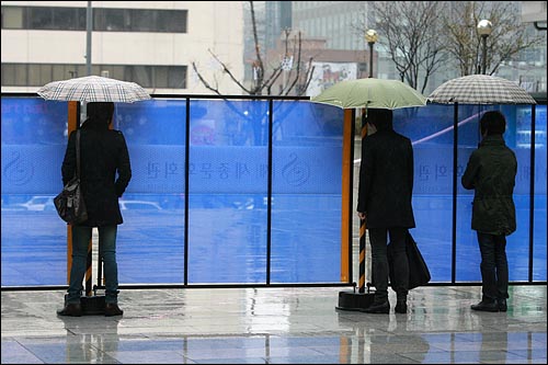  몇몇 시민들이 우산을 가림막에 걸쳐 놓은 채 <아이리스> 촬영장면을 지켜보고 있다.