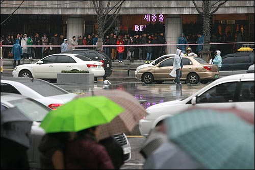  비가 오는 궂은 날씨에도 불구하고 수백명의 시민들이 멀리서 드라마 촬영을 지켜보고 있다.