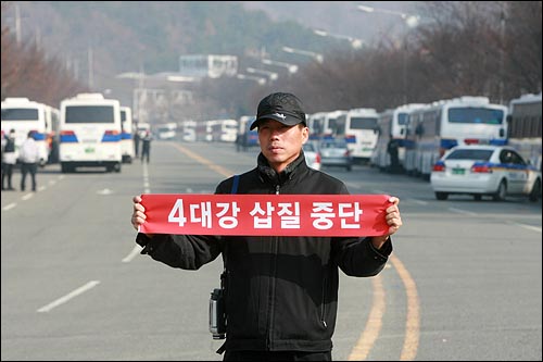 달성보 공사현장앞에서 진보신당 당원이 '4대강 삽질중단' 손피켓을 들고 서 있다.