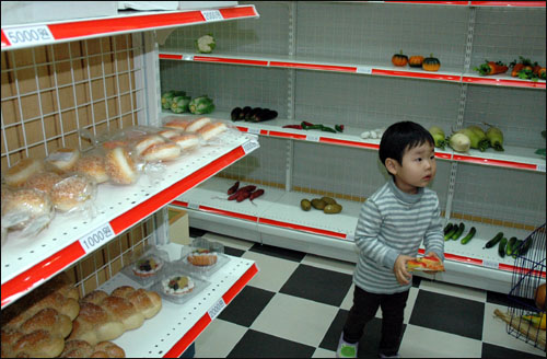 식료품가게에서 한 아이가 모형 물건을 골라 담고 있다.  