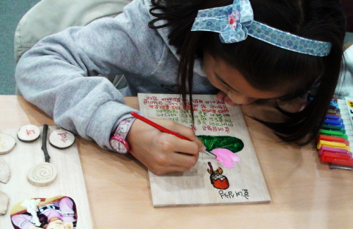 한 초등학생이 나무판에다가 열심히 그림을 그려 넣고 있다. 그 옆엔 자신이 만든 다향한 모양의 책표지가 놓여 있다. 종이 책이 만들어지기 이전의 세상을 상상하면서.