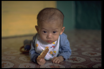 고단백 비스킷을 들고 있는 아기. 북한의 어린이 사망률은 1,000명당 55명에 이르고, 5세 이하 어린이들의 만성적인 영양실조 (37%) 비율이 여전히 높다.