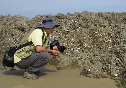 바다에 나간 김준 박사가 카메라를 든 채 쪼그려앉아 바다사람의 이야기를 듣고 있다.