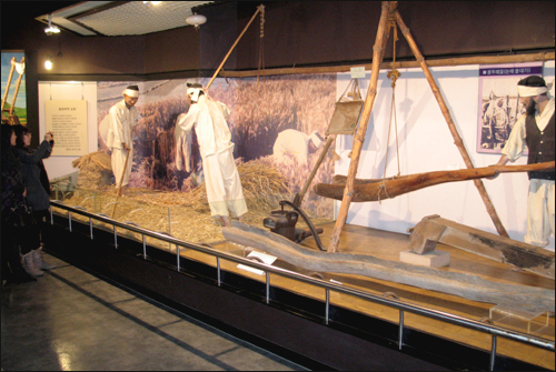 슬비가 농업박물관 전시실에서 곡식 터는 도구들을 카메라에 담고 있다.