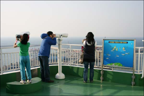 등대 망원경으로 수평선 밖 아스라한 섬과 바다를 조망하는 여행객들