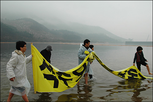 시민단체 회원들이 9일 함안보 공사현장 아래 낙동강에서 시위를 벌이기 위해 대형 펼침막을 들고 들어가고 있다.