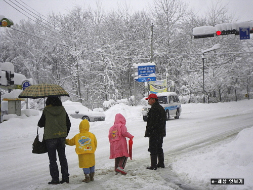 눈 쌓인 도로 위 대중교통을 이용하기 위해 차를 기다리는 가족들