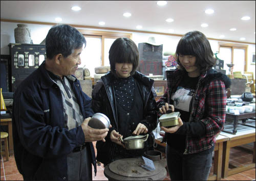 슬비와 예슬이가 김성우 박물관장으로부터 옛날 양은도시락에 얽힌 얘기를 듣고 있다.