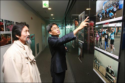<오마이뉴스> 창간 10주년인 22일 오전 오픈하우스 행사가 열리는 서울 상암동 편집국을 방문한 강기갑 민주노동당 대표에게 오연호 대표가 '<오마이뉴스> 주최 2005 평양 마라톤 대회' 사진을 소개하고 있다.