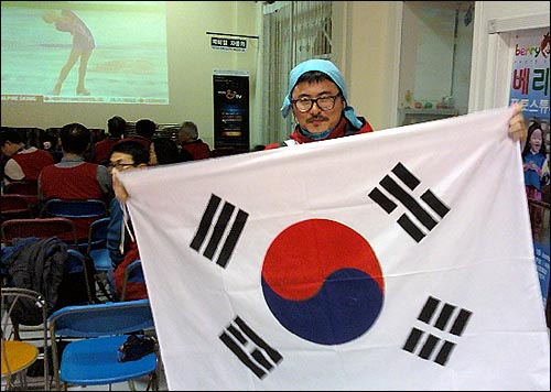 한 교민이 코퀴클람시 한인 플라자에서 태극기를 펴들고 김연아 선수를 응원하고 있다.