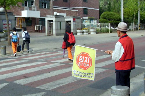 노인 일자리 사업에 참여한 어르신이 초등학교 교통 지도를 하고 있다.
