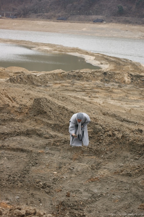지율 스님이 낙동강변에서 오니로 보이는 진흙덩이를 들어 살펴보고 있다