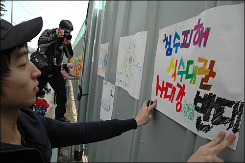 '4대강사업 중단 수륙대재'가 28일 오후 함안보 아래 백사장에서 열렸는데, 어린이들이 '4대강사업 반대'하는 내용이 그림을 그려와 함안보 공사장 가림막에 붙이고 있다.