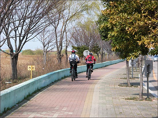 낙동강 자전거도로 위를 달리는 사람들. 왼쪽은 갈대밭, 오른쪽은 산업단지 앞 도로.