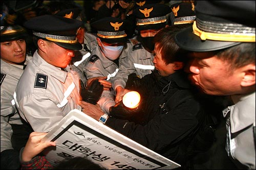 촛불 하나를 뺏기 위해 수십명의 경찰이 몰려 든 가운데 한 경찰이 촛불을 입으로 불어 끄려 하고 있다.