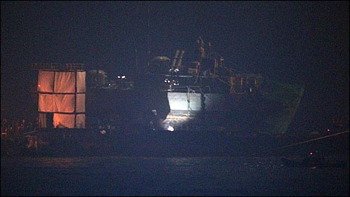 천안함 침몰 20일째인 15일 저녁 백령도 장촌포 함미 인양해역에서 천안함 함미가 바지선 위에 탑재되어 있는 가운데, 군 관계자들이 야간 조명등을 설치해 실종자 시신수습 작업을 벌이고 있다.