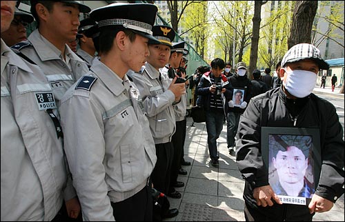  '금양 98호' 실종자 사진을 든 가족들이 정부중앙청사로 걸어가고 있는 가운데 '근조' 리본을 단 경찰들이 청사 주위에 증강배치되어 있다.