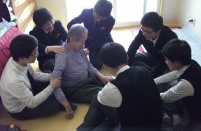 독거노인댁을 방문하여 할머니의 어깨 다리 팔을 주무르고 있는 학생들 