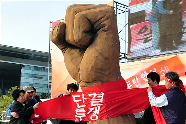 120주년 세계노동절 기념행사에서 전태일 어머니 이소선 여사와 김영훈 민주노총 위원장이 모형 주먹에 '단결투쟁' 띠를 두르는 상징의식을 하고 있다.
