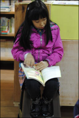 한 여자 아이가 동화책을 집중해 보고 있다. 