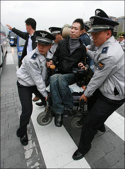 경찰봉쇄를 피해 광화문광장으로 향하는 횡단보도를 건넌 한 장애인이 경찰에 번쩍 들려서 다시 돌아오고 있다.