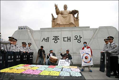4일 오전 서울 광화문 광장 세종대왕 동상앞에서 전국장애인차별철폐연대 소속 회원들이 북을 치며 '장애인 활동보조 살리기 신문고를 울려라' 행사를 벌이자, 경찰들이 이들을 에워싸고 있다.