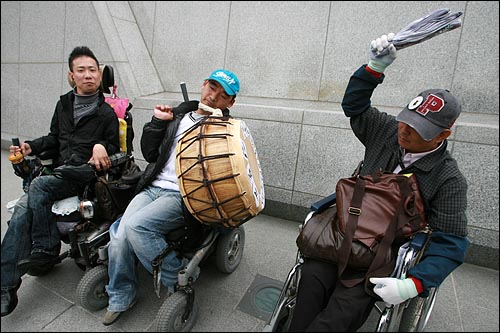 경찰에게 북채를 뺏긴 장애인들이 신문지를 뭉쳐서 북을 계속치고 있다.