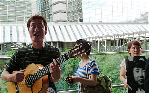 가수인 히라다 요시오씨가 미쓰비시 본사 앞에서 <힘 내세요 할머니>라는 곡을 부르고 있다. 이 노래는 근로정신대 할머니들을 위해 만든 노래다.