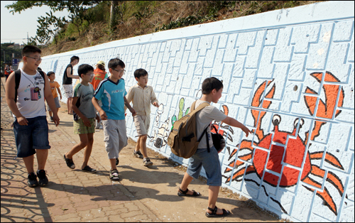  건양대학교 ‘아트애드’ 동아리 학생들이 도로변 옹벽에 ‘바닷속 풍경’ 벽화를 완성했다. 사진은 고남초 학생들이 벽화를 보며 즐거워하고 있는 모습.