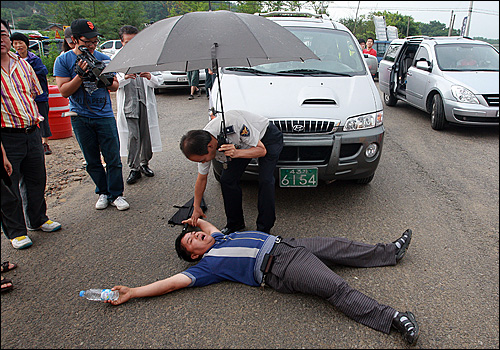 김상희 민주당 의원과 홍희덕 민주노동당 의원, 유원일 창조한국당 의원이 농성자들을 만나기 위해 차를 타고 공사현장으로 들어가려 하자 4대강 사업을 찬성하는 한 시민이 바닥에 드러누워 차량 진입을 막고 있다.
