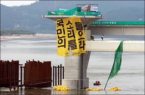  박평수 고양환경연합 집행위원장이 '국민의 소리를 들으라'가 적힌 대형 홍보 현수막을 풀어 낸 뒤 농성장으로 다시 올라가기위해 로프에 매달려 있다.