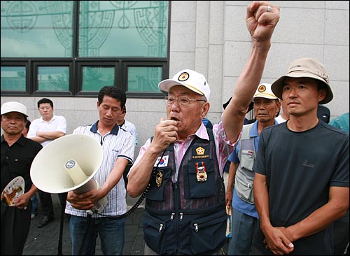 4대강 사업 반대 집회를 위해 준비된 마이크를 잡은 '6.25국가유공자' 마크와 훈장을 단 찬성단체 회원이 '대통령을 중심으로 똘똘 뭉쳐야 한다"고 주장하고 있다.