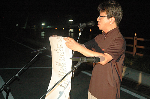 환경연합 두 활동가가 함안보 공사장 철탑에서 고공농성을 한 지 17일째인 7일 저녁 합안보 홍보관 옆에서 열린 촛불문화제에서 김유철 시인이 시를 낭송하고 있다.