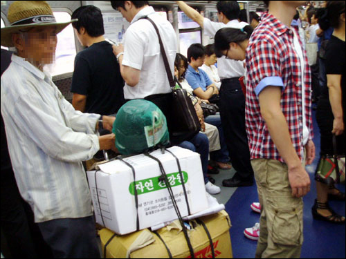 지하철 1호선 열차 안에 채소 박스를 든 노인이 서 있다.