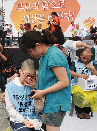 31일 오후 서울 종로구 보신각 앞에서 열린 '장애인부모 전국집중결의대회'에서 장애자녀를 둔 부모들이 장애인 복지 예산 확보와 장애아동 및 발달장애인의 권리보장을 촉구하며 삭발하자 참석자들이 포옹하며 격려하고 있다.