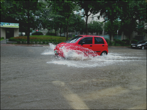 아파트 단지 도로에 순식간에 빗물이 차 소형차는 바퀴가 물에 잠겨 떠 가는듯 하다. 