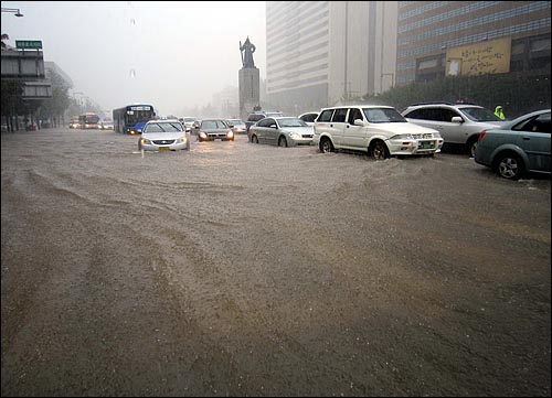 21일 오후 서울 도심에 내린 폭우로 인해 호수처럼 변한 광화문네거리를 버스와 승용차들이 지나고 있다.